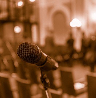 Microphone in focus against blurred chairs and standing talking audience